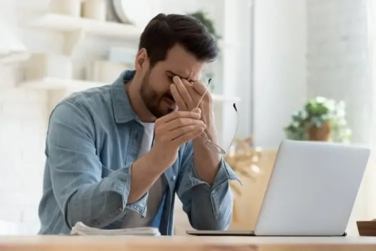Homme devant un écran souffrant de fatigue oculaire à cause d’une exposition prolongée aux écrans